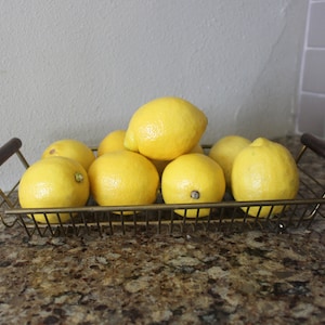 May include: A gold wire basket with wooden handles filled with eight yellow lemons.