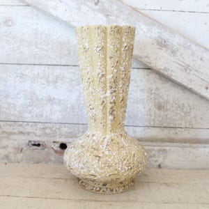 May include: A tall, textured vase with a bulbous base and a fluted neck. The vase is a light beige color with a speckled, rough surface. It stands approximately 12 inches tall and is suitable for floral arrangements.