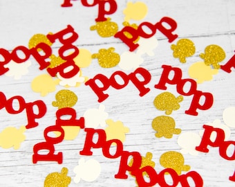 May include: Red and gold confetti with the word "Pop" repeated on each piece. The confetti is scattered on a white wooden surface.
