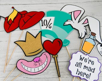May include: A set of 10 Alice in Wonderland themed photo booth props. The props include a crown, a heart, a Cheshire cat grin, a Mad Hatter hat, a bottle, a rabbit, and a sign that says "We're all mad here!"