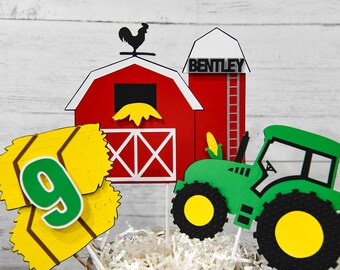 May include: A farm-themed cake topper set featuring a red barn with a black rooster weather vane, a silo labeled BENTLEY, a green tractor with yellow wheels, and a yellow hay bale cutout displaying the green number 9 on white sticks.
