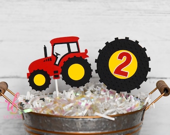 May include: Red toy tractor with yellow wheels and a black tire with the number 2 on it. The tractor and tire are on sticks and are in a metal bucket with white and iridescent shredded paper.
