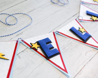 May include: A blue and white banner with the letter "E" and a yellow star on each triangle. The banner is strung with twine.