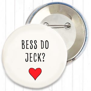 Könnte beinhalten: Ein weißer Ansteckbutton mit dem schwarzen Text "BESS DO JECK?" und einem roten Herz. Der Button ist rund und hat eine Nadel auf der Rückseite.