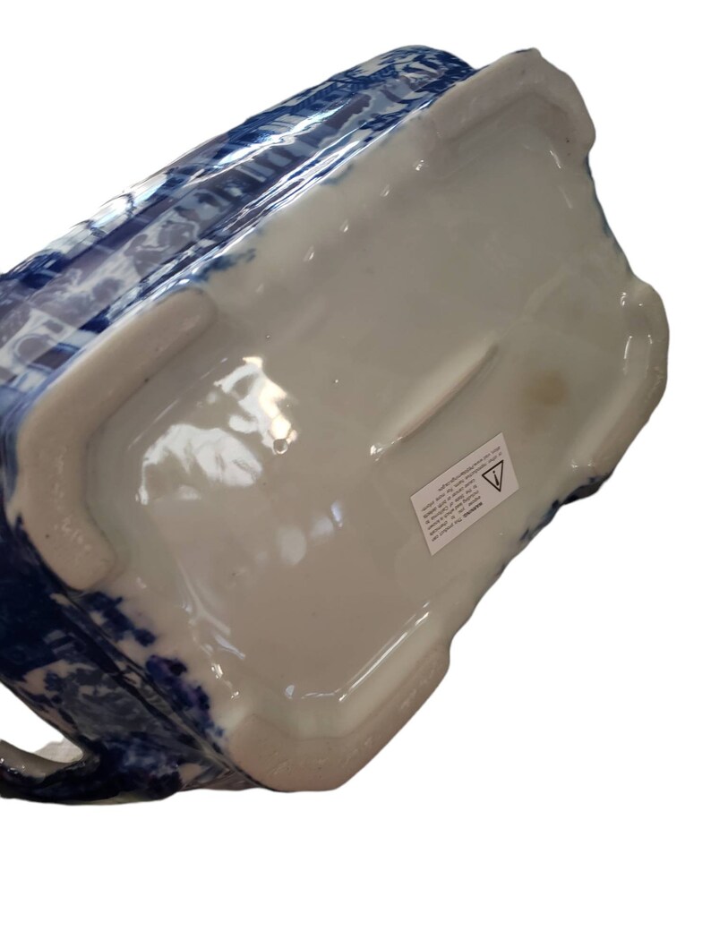 May include: A ceramic pitcher with a blue and white floral pattern. The pitcher has a rectangular shape with a handle and a white interior. The bottom of the pitcher is white with a sticker.