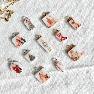 May include: A collection of small, white, rectangular, square, and oval-shaped jewellery charms featuring various Christmas-themed illustrations, including Santa Claus, a nutcracker, a Christmas tree, gifts, and a dog, paired with a gold chain.