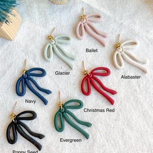 May include: Ten pairs of bow-shaped earrings in various colors, including navy, black, green, red, white, and light blue. Each earring features a gold post.