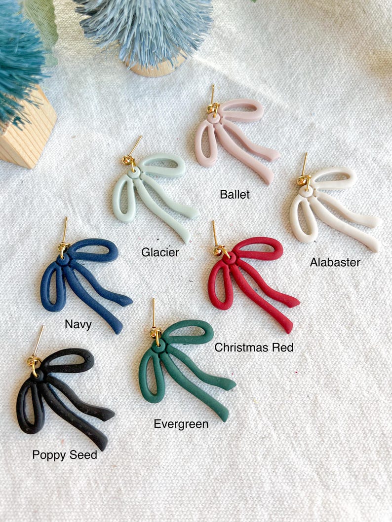 May include: Ten pairs of bow-shaped earrings in various colors, including navy, black, green, red, white, and light blue. Each earring features a gold post.