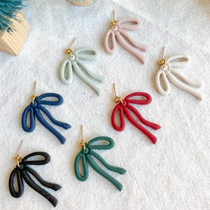 May include: Assortment of six pairs of bow-shaped earrings in various colors, including black, navy blue, green, red, light blue, and pink. The earrings are made of polymer clay and have a gold-tone post.