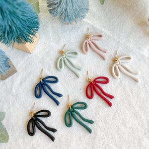 May include: Eight pairs of bow-shaped earrings in various colors, including pink, green, blue, red, and black. The earrings are made of polymer clay and have a gold-tone hook.