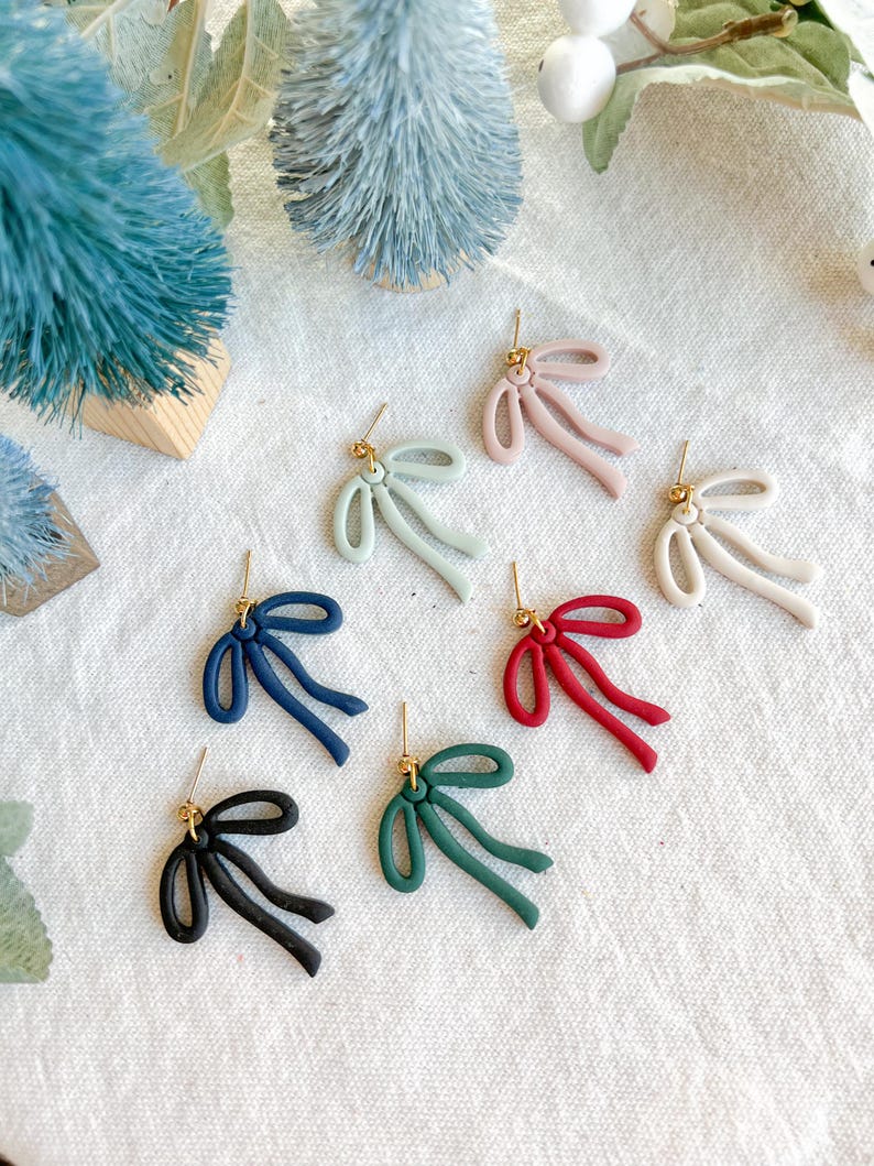 May include: Eight pairs of bow-shaped earrings in various colors, including pink, green, blue, red, and black. The earrings are made of polymer clay and have a gold-tone hook.