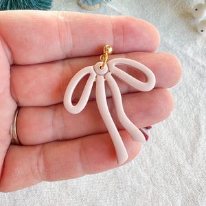 May include: A pair of pink polymer clay earrings shaped like a bow with a gold hook.