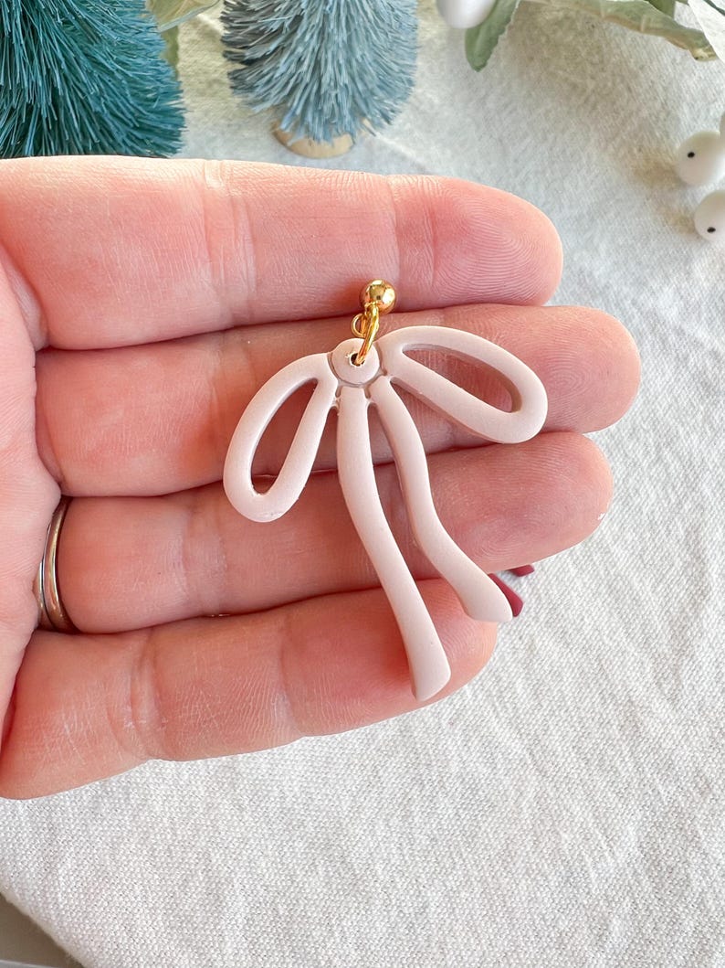 May include: A pair of pink polymer clay earrings shaped like a bow with a gold hook.