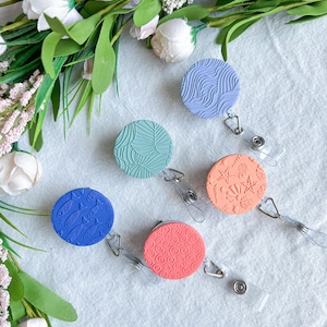 May include: Five different patterned badge reels with retractable cords. The reels are blue, green, orange, and red with various designs including fish, leaves, and swirls.