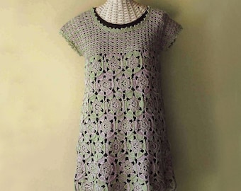 Peut inclure: Une tunique en crochet à manches courtes avec un motif floral répétitif dans des tons vert clair et lavande. Le vêtement présente une encolure ronde et est superposé sur une base noire unie, révélant un motif ajouré complexe.