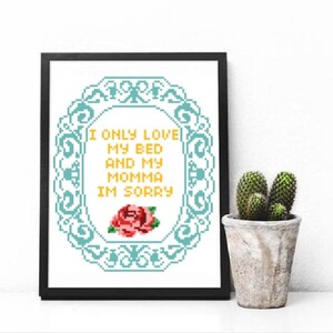 May include: A framed cross-stitch design with a blue and white floral border. The text inside the frame reads "I only love my bed and my momma I'm sorry". A red rose is centered below the text.