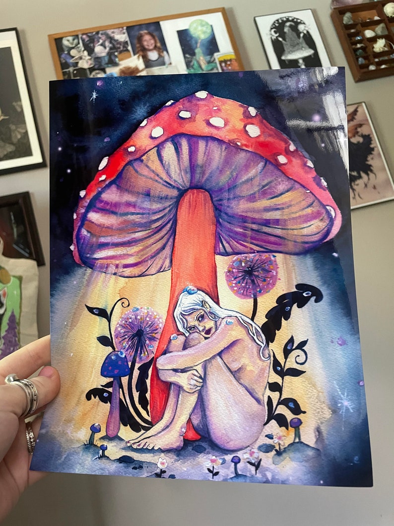 May include: A watercolor painting of a nude woman sitting under a large, red and purple mushroom with white spots. The woman has long, white hair and is holding her knees. The background is a dark blue with stars and a few small, purple mushrooms.