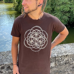 May include: A brown t-shirt with a white geometric design printed on the front. The design is a circle with a flower-like pattern inside.