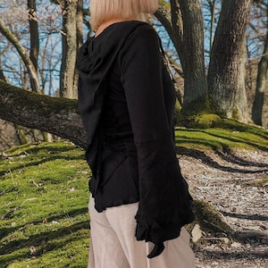 Op de afbeelding: Een zwart hooded top met lange mouwen en geruite randen. De top heeft een getailleerde taille en een vloeiende, gedrapeerde capuchon. Het model draagt de top met een beige broek.