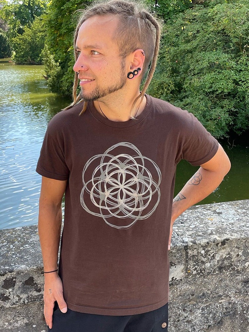 May include: A brown t-shirt with a white geometric design printed on the front. The design is a circle with a flower-like pattern inside.