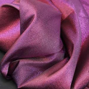 May include: Close-up of a shimmering iridescent fabric in shades of purple and pink. The fabric has a subtle texture and a soft, flowing drape.