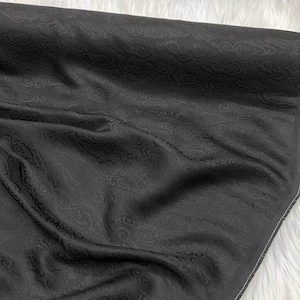 May include: Black fabric with a raised cloud pattern. The fabric is folded and has a white edge.