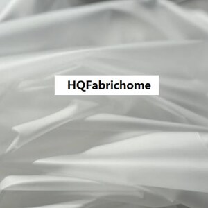 K&ouml;nnte beinhalten: Wei&szlig;er Stoff mit einer glatten, seidenartigen Textur. Der Stoff ist gefaltet und drapiert, wodurch weiche Falten und Kurven entstehen. Der Text "HQFabrichome" ist auf den Stoff gedruckt.