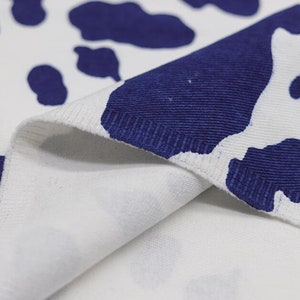 K&ouml;nnte beinhalten: Nahaufnahme eines wei&szlig;en Stoffes mit einem blauen Kuhmuster. Der Stoff ist umgeklappt, sodass die Unterseite des Materials sichtbar ist.