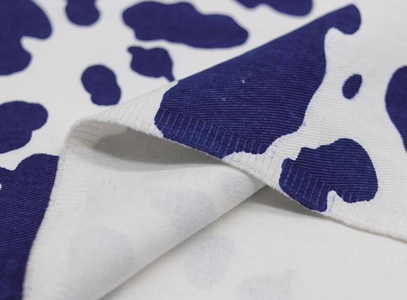 K&ouml;nnte beinhalten: Nahaufnahme eines wei&szlig;en Stoffes mit einem blauen Kuhmuster. Der Stoff ist umgeklappt, sodass die Unterseite des Materials sichtbar ist.