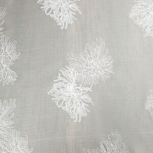 May include: A sheer light gray fabric featuring an embroidered pattern of white chrysanthemum flowers. The delicate floral design is repeated across the surface, showcasing intricate line work that defines each petal of the blossoms.