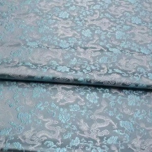 May include: A light blue fabric with a white brocade pattern of dragons and flowers.