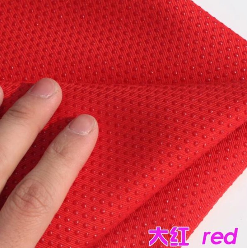 Pu&ograve; includere: Primo piano di un tessuto rosso con una superficie testurizzata. Il tessuto presenta piccoli punti in rilievo che creano una texture irregolare. Il tessuto &egrave; piegato a met&agrave; e la piega &egrave; visibile nell'immagine.