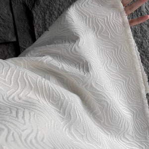May include: White fabric with a textured, wavy pattern. The fabric is soft and has a subtle sheen.