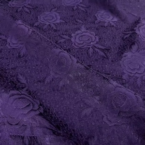 May include: Close-up of a deep purple fabric with a floral pattern. The fabric features embossed roses and leaves, creating a textured surface. The design is repeated across the material, showcasing a classic, elegant style.
