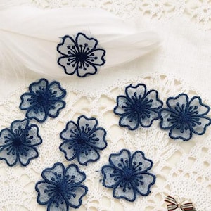 Può includere: Sette applicazioni floreali blu con un delicato disegno in pizzo. Le applicazioni sono realizzate in un tessuto trasparente e hanno un leggero bagliore.