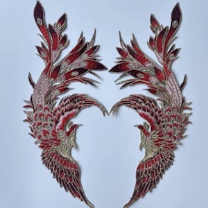 May include: Pair of embroidered patches featuring a phoenix design. The patches showcase a vibrant color palette of red, burgundy, and gold. The intricate embroidery details the feathers and form of the mythical bird. These patches are ideal for adding a decorative touch to clothing or accessories.