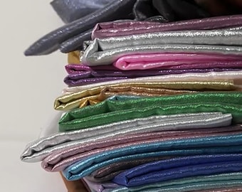 May include: A stack of folded fabric in various colors, including silver, pink, gold, green, and blue. The fabric has a shiny, metallic appearance, suggesting it may be used for clothing or decorative purposes. The stack is neatly arranged, showcasing the different hues.