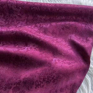 May include: A close-up of a deep purple fabric with a white floral pattern. The fabric has a soft, silky texture.