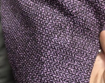 May include: Close-up of a textured fabric with a woven pattern. The fabric is mainly dark purple with small flecks of lighter purple and black, creating a subtle, intricate design. The material appears soft and possibly suitable for clothing or upholstery.