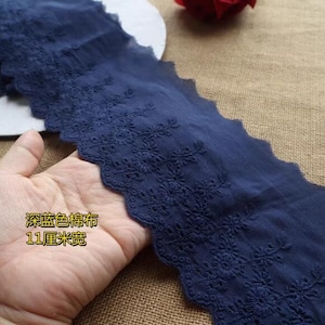 May include: Navy blue embroidered cotton fabric with a scalloped edge. The fabric features delicate floral embroidery along one edge. The text on the fabric reads: "Dark blue cotton fabric, 11 cm wide."