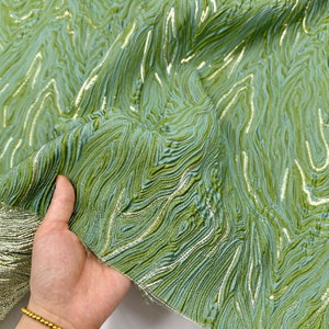 May include: Green fabric with a metallic silver swirl pattern. The fabric has a textured, woven look.