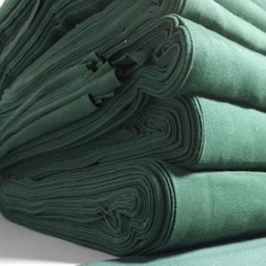 Peut inclure: Gros plan sur des rouleaux de tissu vert empilés. Le tissu est d'une couleur verte unie et profonde et semble doux. Les bords du tissu sont visibles, montrant les couches des rouleaux.