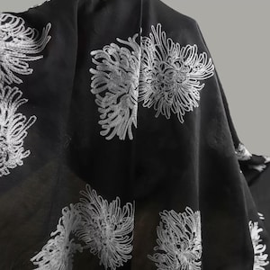 May include: A black fabric textile featuring a repeating pattern of white embroidered chrysanthemum flowers. The material is lightweight and semi-sheer, with the intricate white thread work creating a high-contrast floral design across the surface.