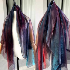 May include: A sheer iridescent scarf with a gradient of red, blue, and teal colors. The scarf is draped over a mannequin.