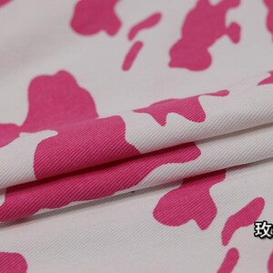 K&ouml;nnte beinhalten: Wei&szlig;er Stoff mit einem pinkfarbenen Kuhmuster. Der Stoff ist in der Mitte gefaltet und der Text "玫红" ist in der unteren rechten Ecke sichtbar.