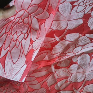 Może przedstawiać: Czerwony materiał z białym wzorem kwiatowym. Materiał ma fakturę w reliefie, nadając kwiatom efekt 3D.