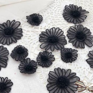 May include: A collection of black sheer fabric flower appliques. The flowers have a daisy shape with multiple layers of petals.