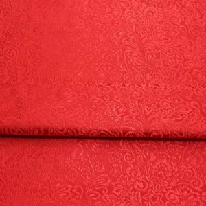 Puede incluir: Tela roja con un patrón floral en relieve. La tela está doblada por la mitad, mostrando el patrón en ambos lados.