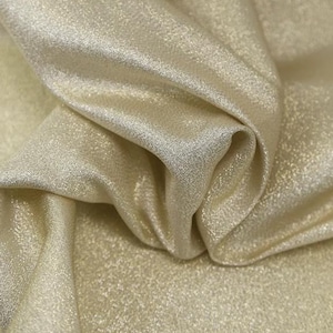 May include: A close-up of a soft, shimmery, gold fabric with a subtle sparkle. The fabric has a smooth texture and a luxurious feel.
