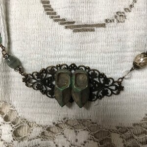 May include: A necklace with a bronze filigree pendant featuring two miniature green shoes. The necklace also has green and clear beads.